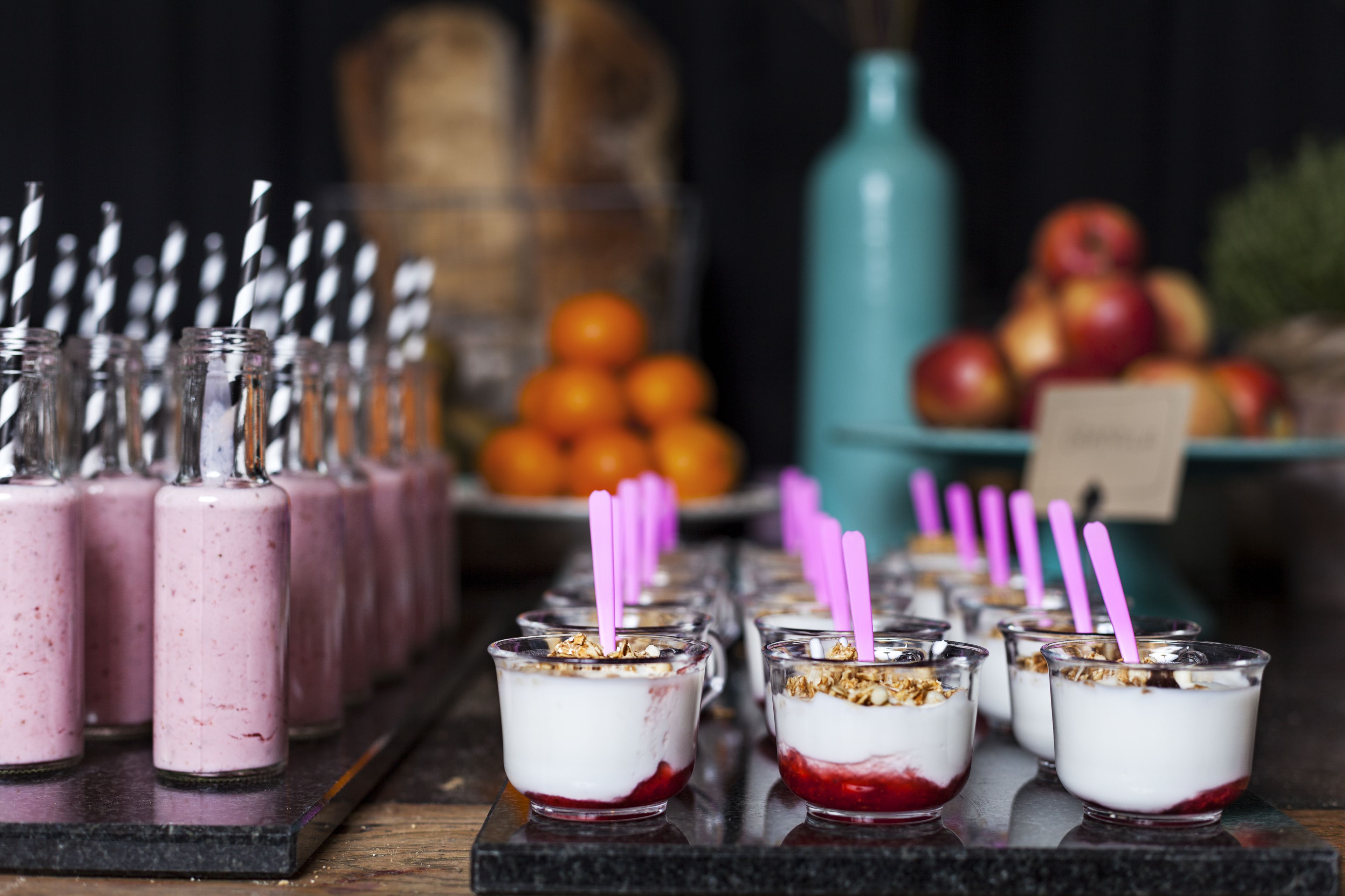A series of small glasses with layered desserts and purple straws, arranged on a wooden surface.