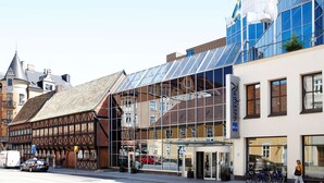 A modern building with a glass facade and a traditional half-timbered structure adjacent to it.