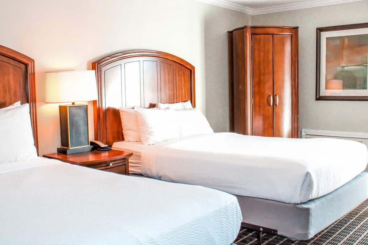 A hotel room with two beds, a nightstand with a lamp, a telephone, and a wardrobe.