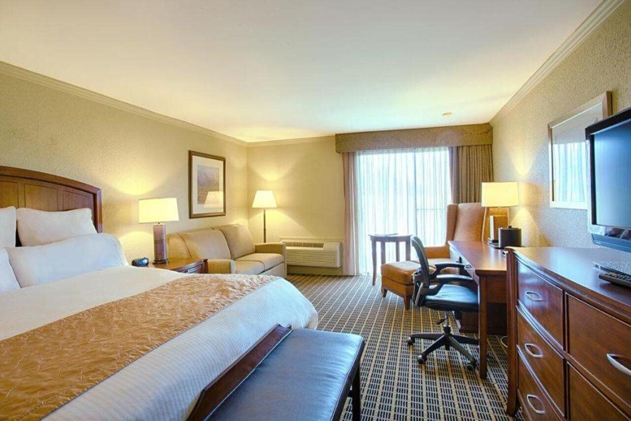 A hotel room with a large bed, a desk with a computer, a chair, a television, and a window with curtains.