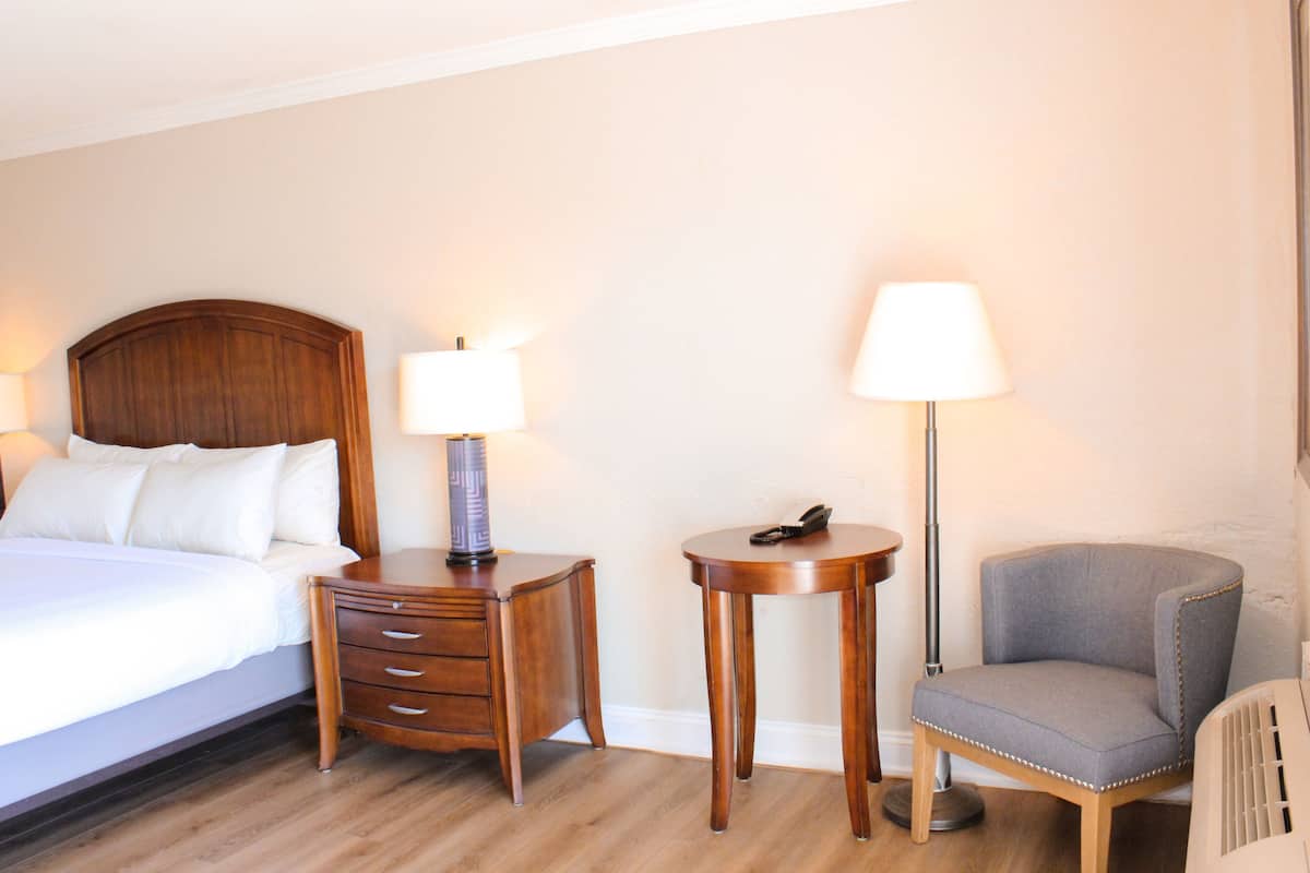 A hotel room with a bed, a nightstand with a lamp, a small table with a lamp, and a chair.
