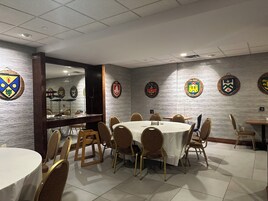 Un salón de conferencias con mesas y sillas redondas, un revestimiento de madera decorativo y varios escudos en la pared.