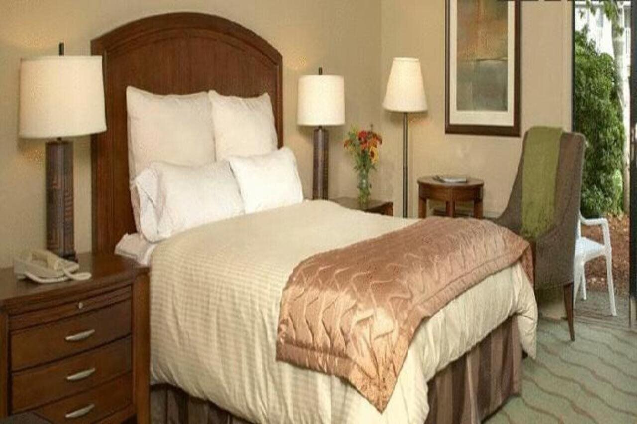 Ein Hotelzimmer mit einem Bett, Nachttischlampen, einem Sessel, einem Nachttisch und einem gerahmten Bild an der Wand.