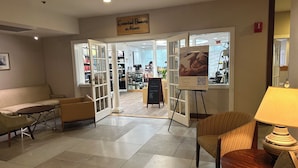 A lobby with a sofa, chairs, a table, a sign reading "Essential Beauty at Atlantis," and a view into the spa area. - Cape Cod Irish Village (Hyannis)