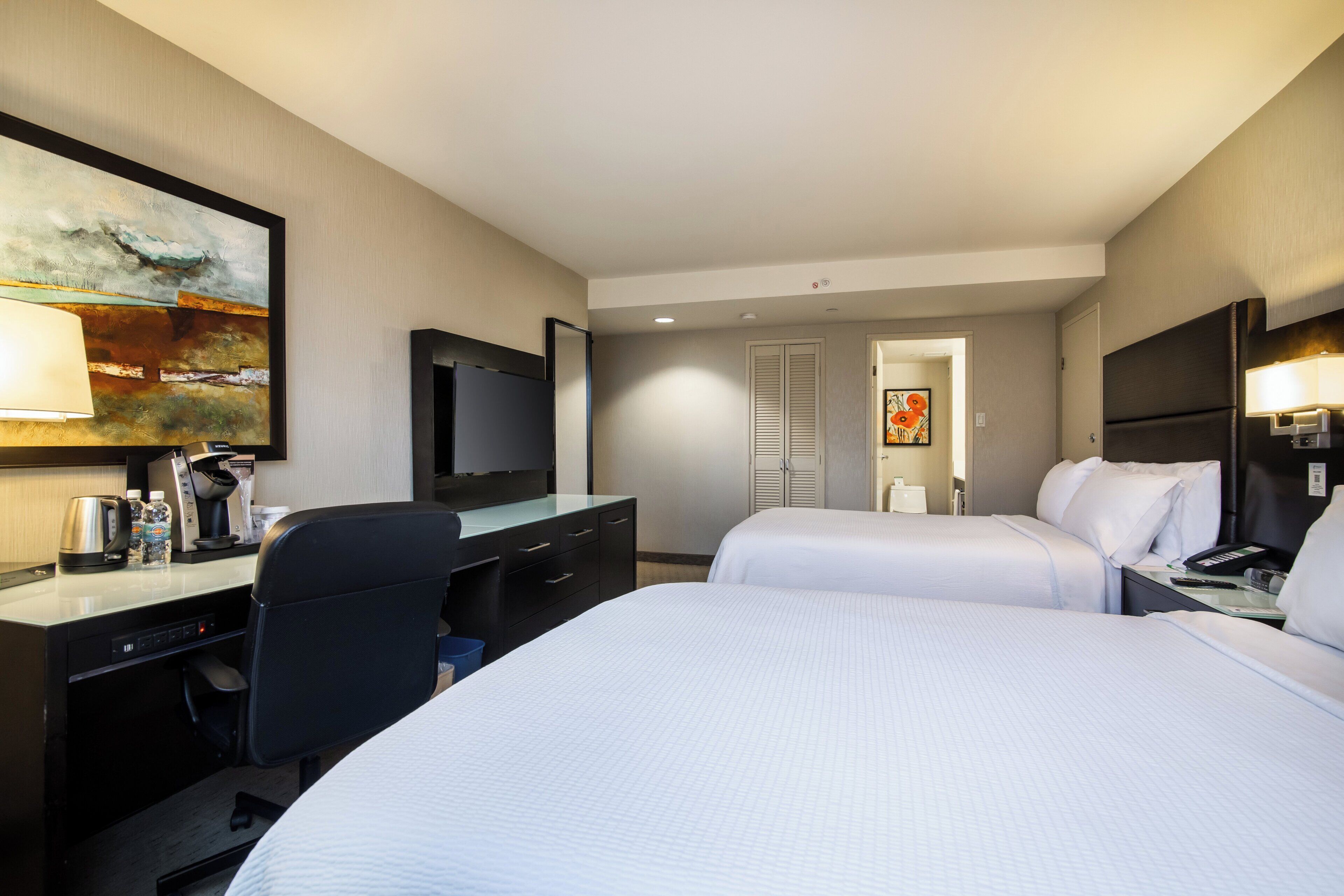 Une chambre d’hôtel équipée d’un lit, d’un bureau, d’une chaise, d’une télévision et d’œuvres d’art.