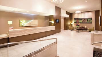 A hotel reception area with a marble counter, a digital screen, and a seating area with chairs and a sofa.