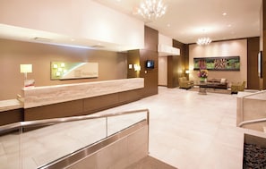 A hotel reception area with a marble counter, a digital screen, and a seating area with chairs and a sofa. - Holiday Inn Vancouver Centre by IHG (Vancouver)