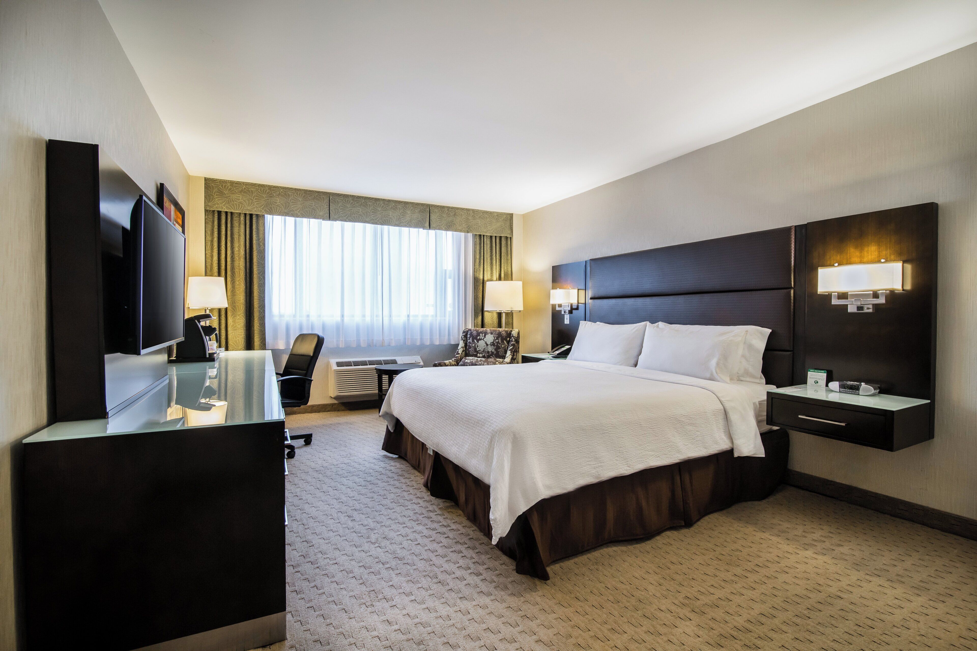 Habitación de hotel con cama, mesitas de noche, un escritorio con silla, televisor y ventana con cortinas.