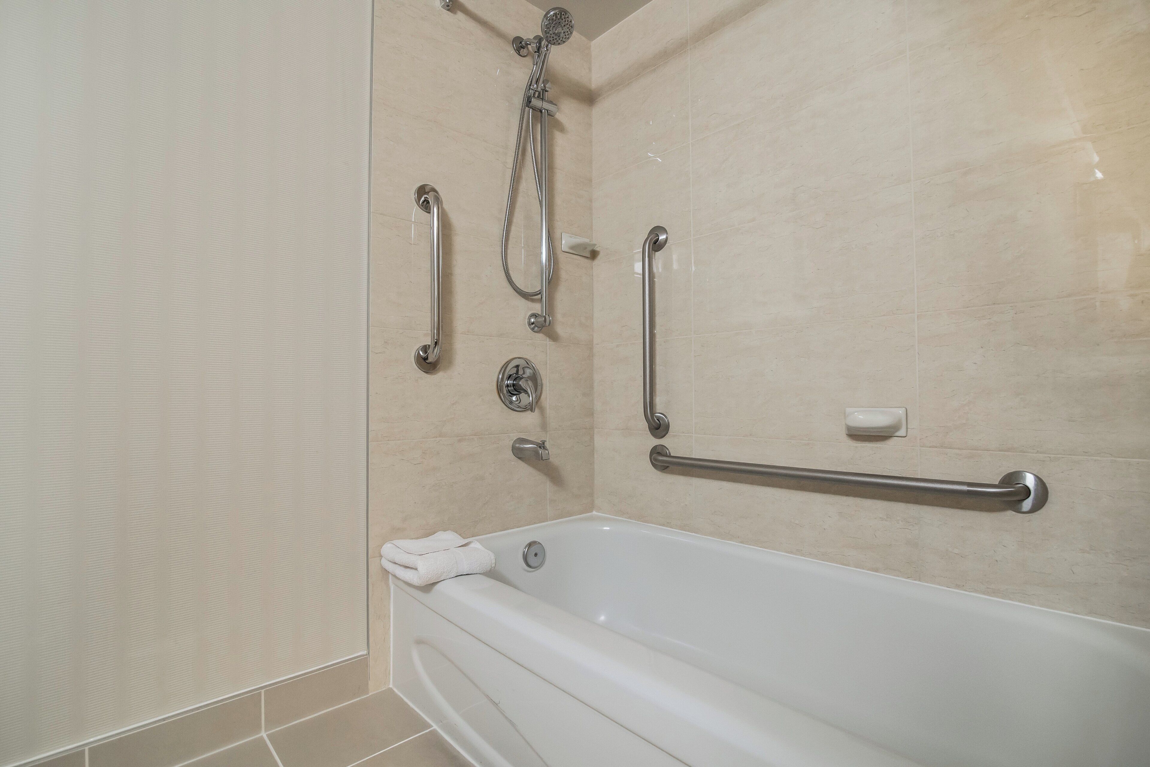A bathroom with a bathtub, grab bars, and a shower head.
