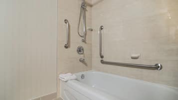 A bathroom with a bathtub, grab bars, and a shower head.