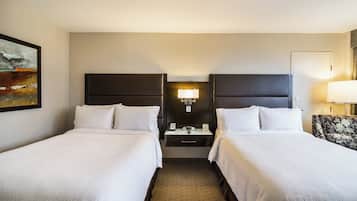 A hotel room with two beds, a nightstand, a lamp, and a painting on the wall.