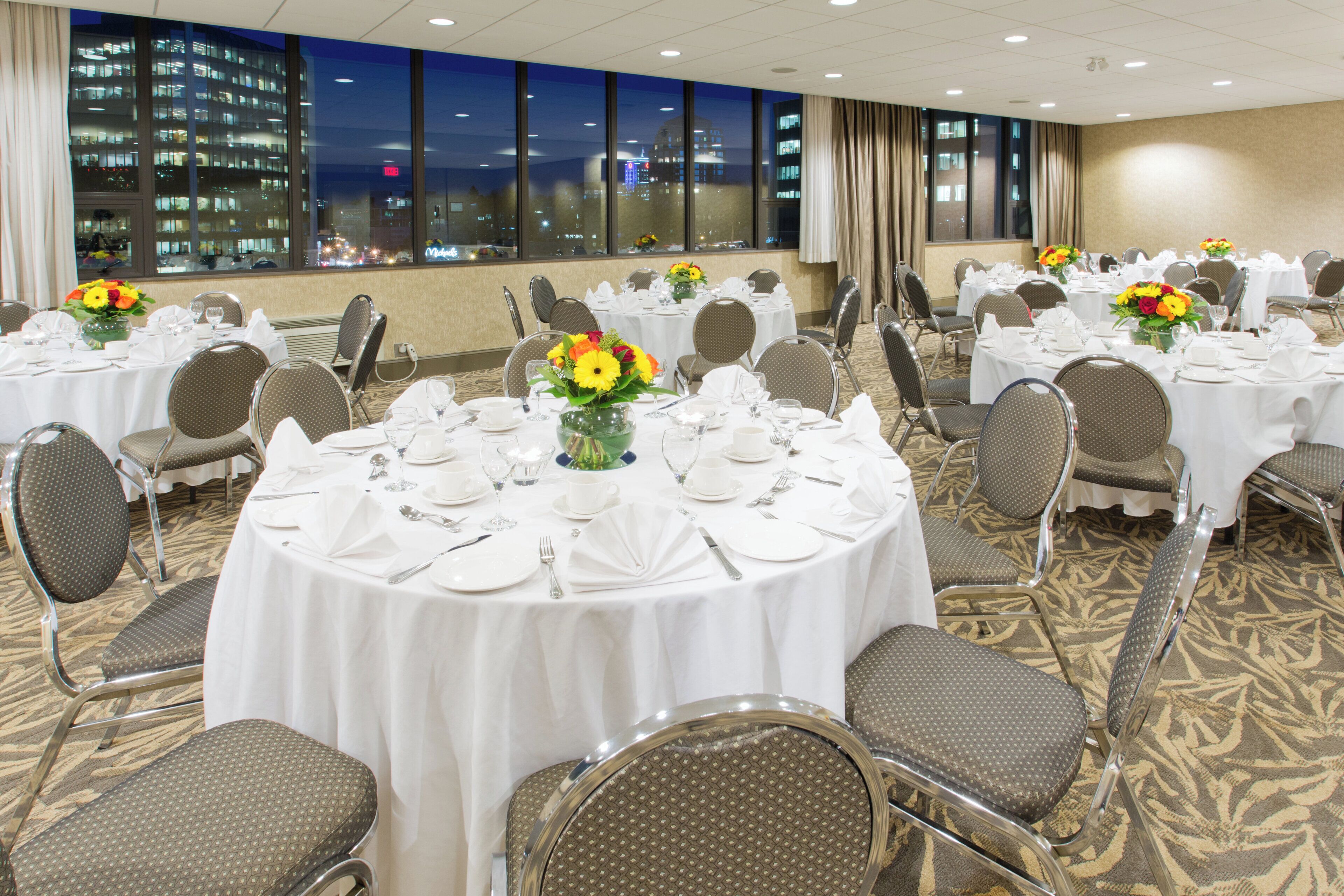 A conference room with round tables, chairs, and floral centerpieces.