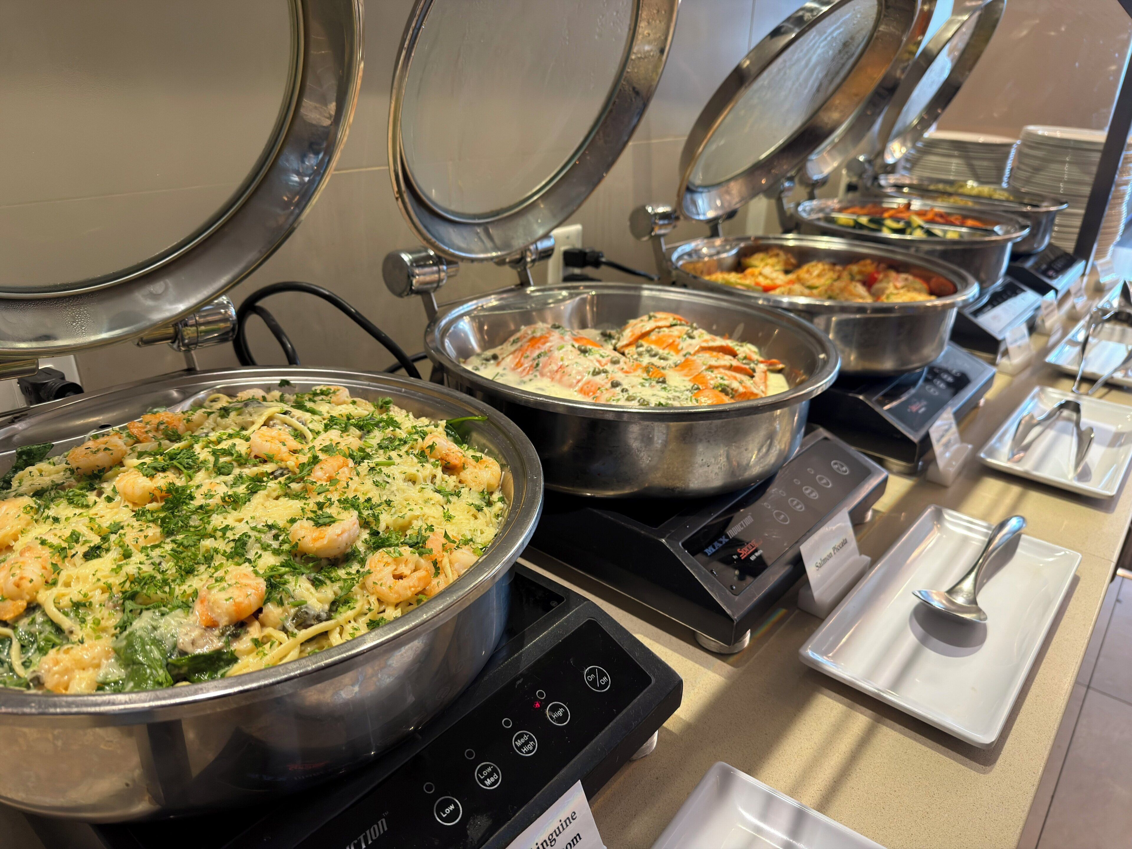 Un buffet proposant divers plats, notamment des pâtes aux fruits de mer et un plat crémeux aux fruits de mer, servis dans de grands récipients en métal.