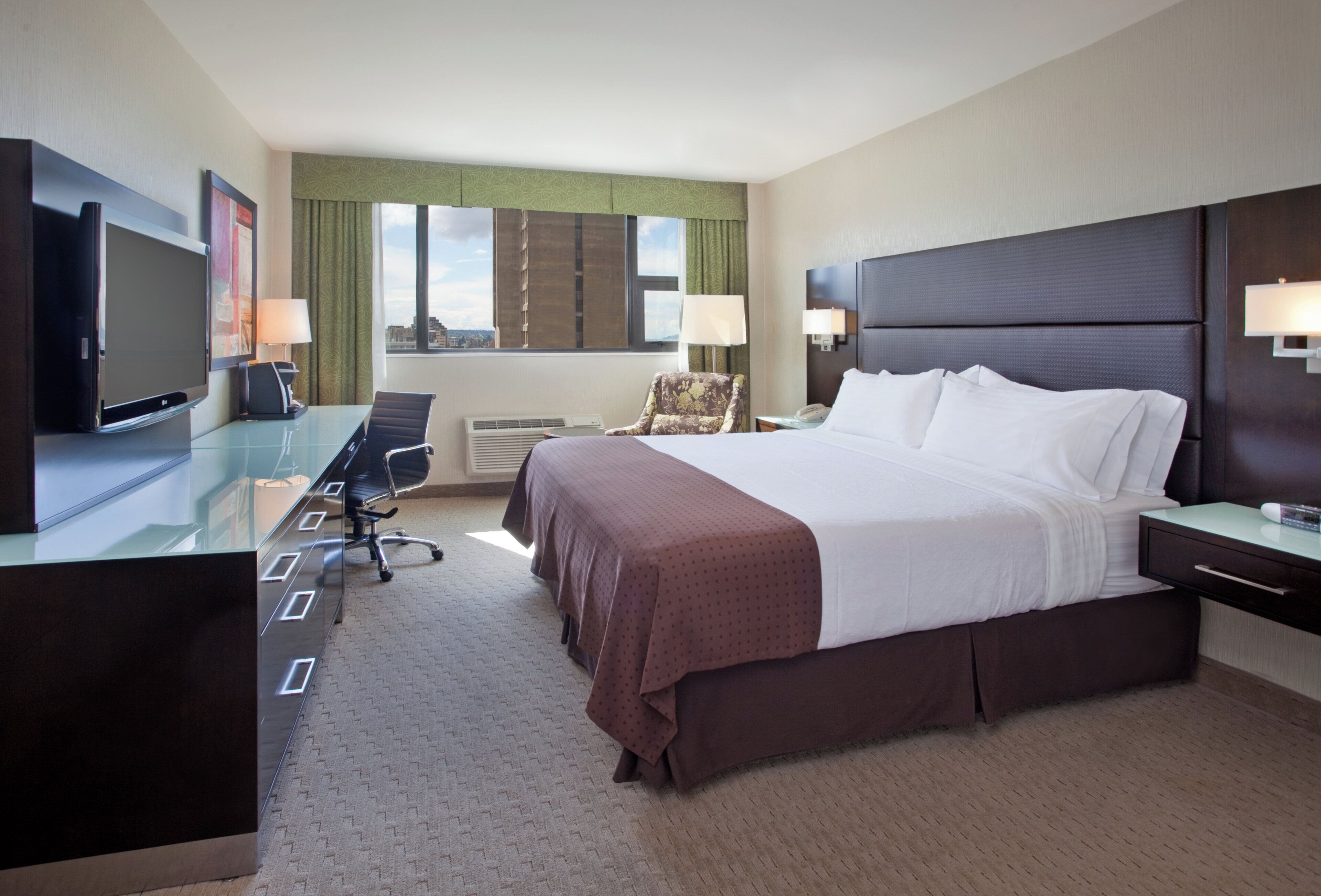 A hotel room with a large bed, a desk with a chair, a television, and a window with curtains.