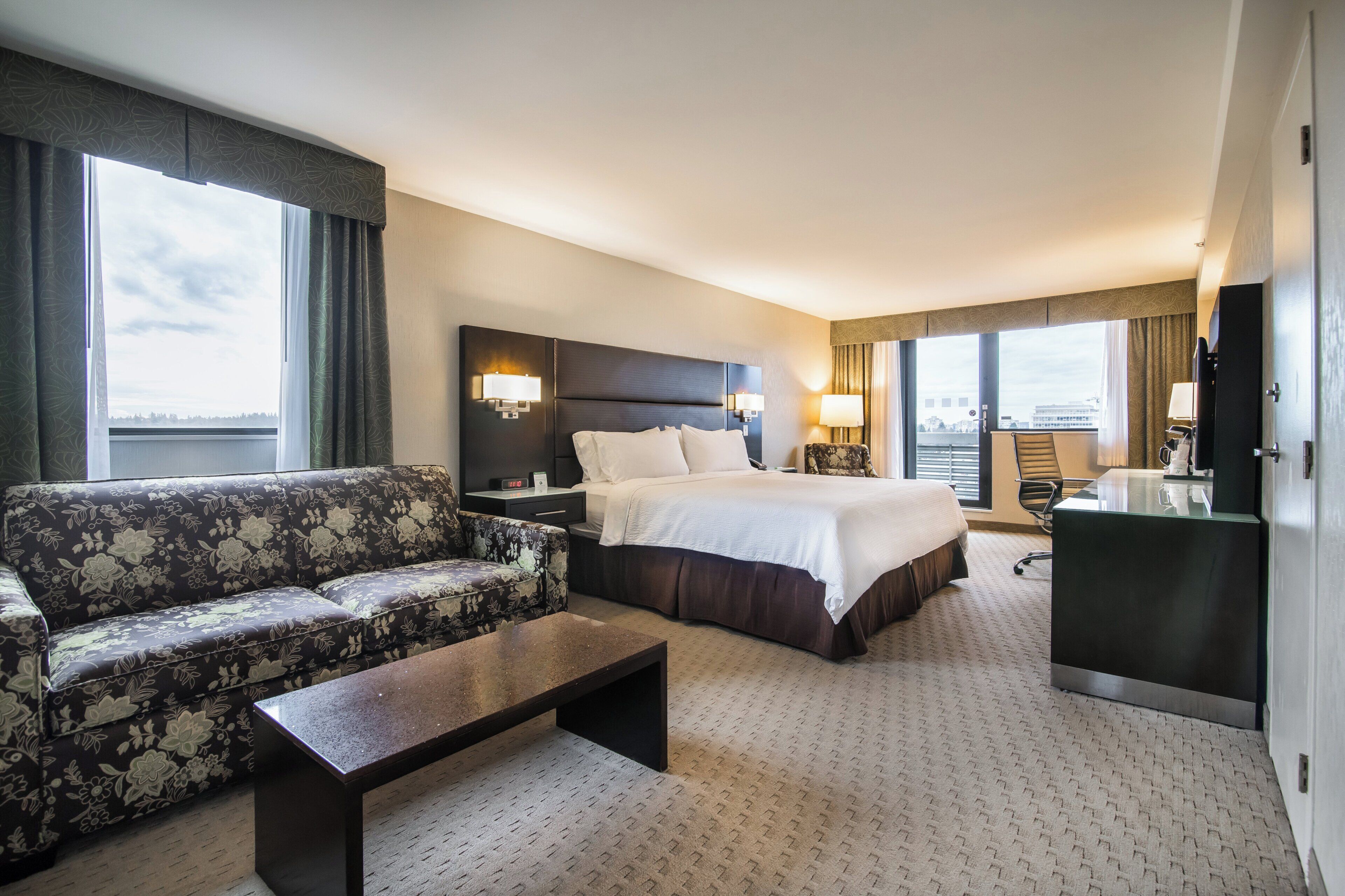 Habitación de hotel con cama, sofá, escritorio y vistas a la ciudad.