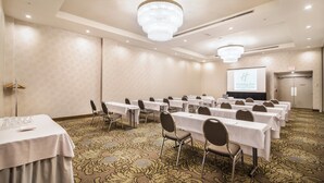 Un salón de conferencias con mesas y sillas, una araña y una pantalla de proyección que muestra el logotipo de Holiday Inn.