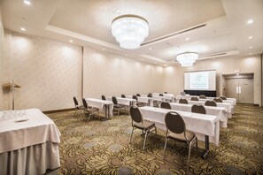 A conference room with tables and chairs, a chandelier, and a projection screen displaying the Holiday Inn logo.