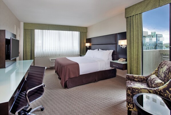 A hotel room with a bed, a desk, a chair, a TV, and a window with curtains.