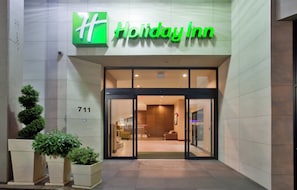 A Holiday Inn hotel entrance with a glass door, a number 711 sign, and potted plants on the left. - Holiday Inn Vancouver Centre by IHG (Vancouver)