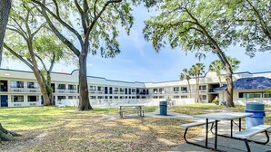 A courtyard with picnic tables, a trash bin, and a building with multiple balconies and windows. - Stayable Kissimmee West (Kissimmee)