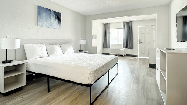 A modern hotel room with a large bed, bedside tables, a desk, and a television. - Stayable Kissimmee West (Kissimmee)