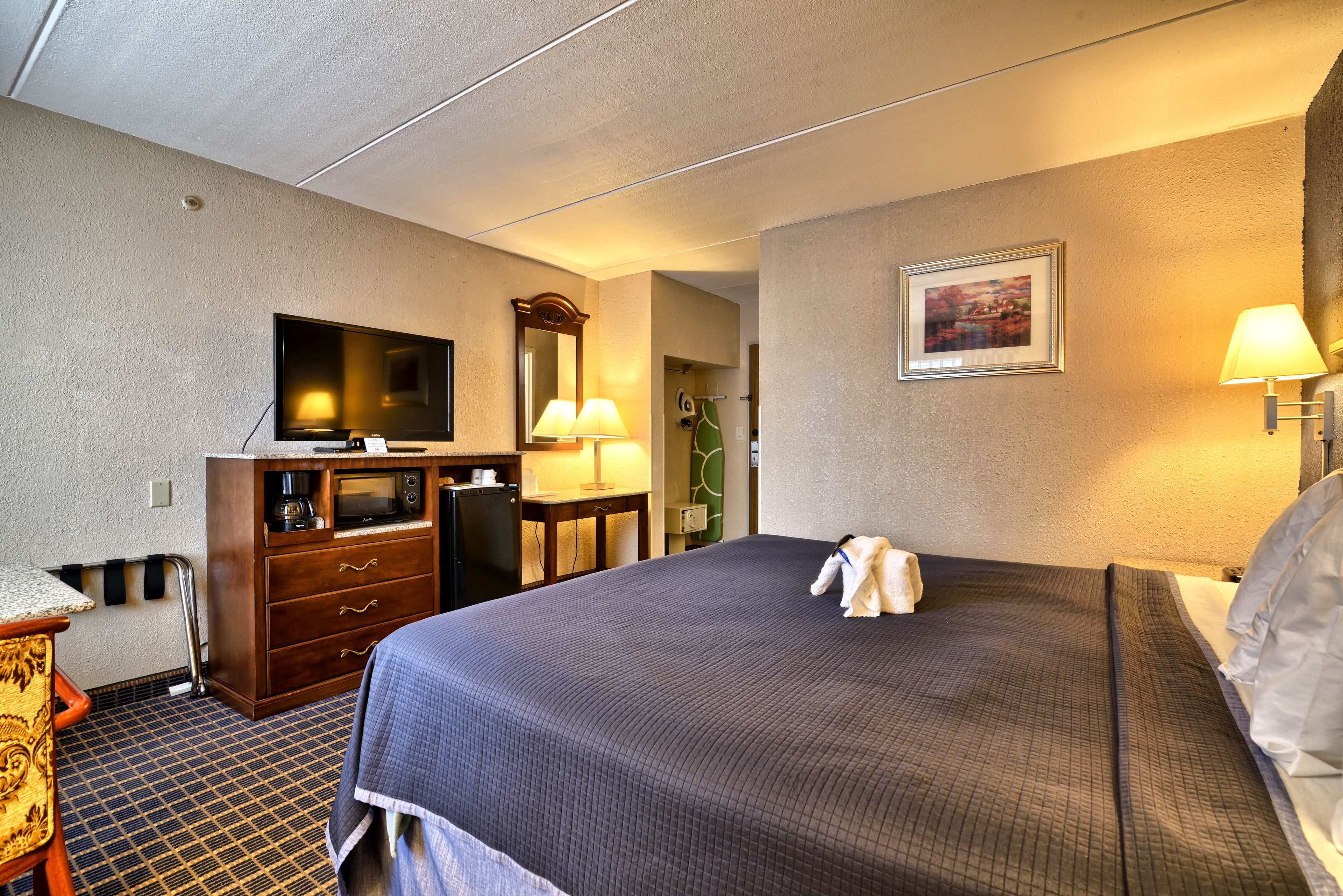 Una habitación de hotel con cama, escritorio, televisor de pantalla plana, microondas y cómoda.