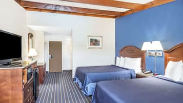 Habitación de hotel con dos camas, un televisor, un escritorio con lámpara y una puerta que da a otra habitación.