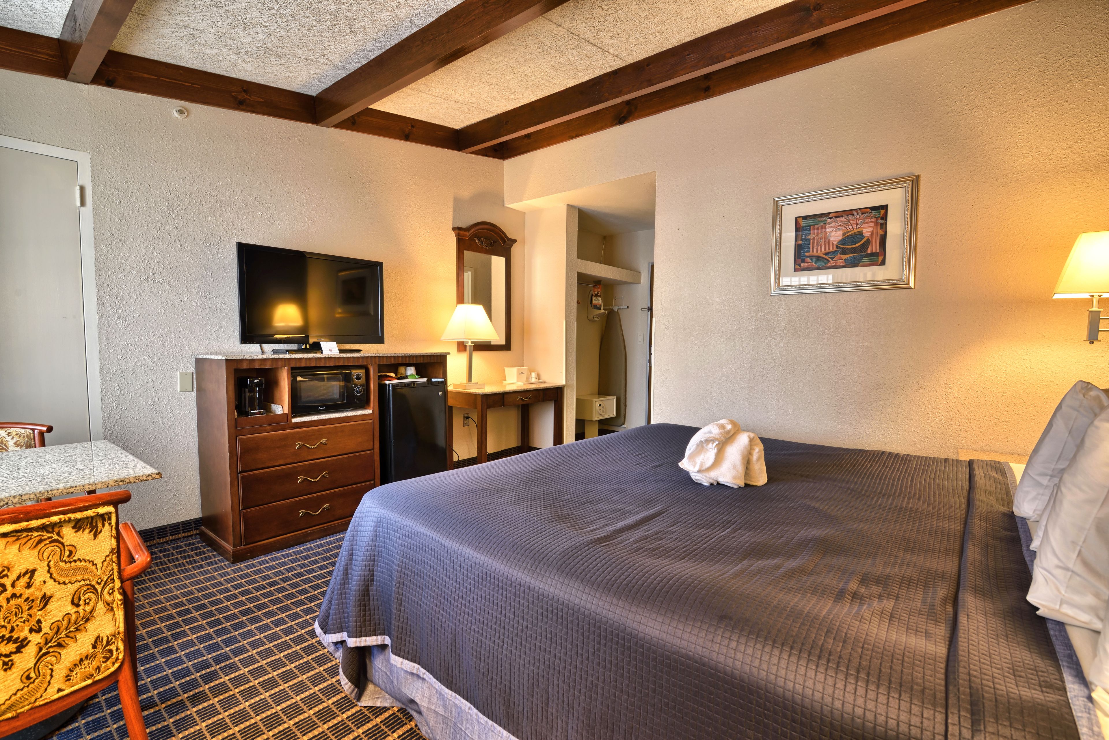 A hotel room with a bed, a television, a desk with a chair, a microwave, and a bathroom visible through an open door.