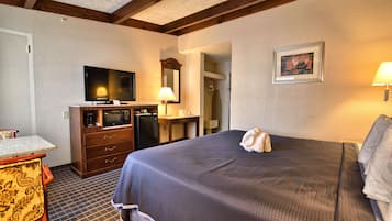 A hotel room with a bed, a television, a desk with a chair, a microwave, and a bathroom visible through an open door.