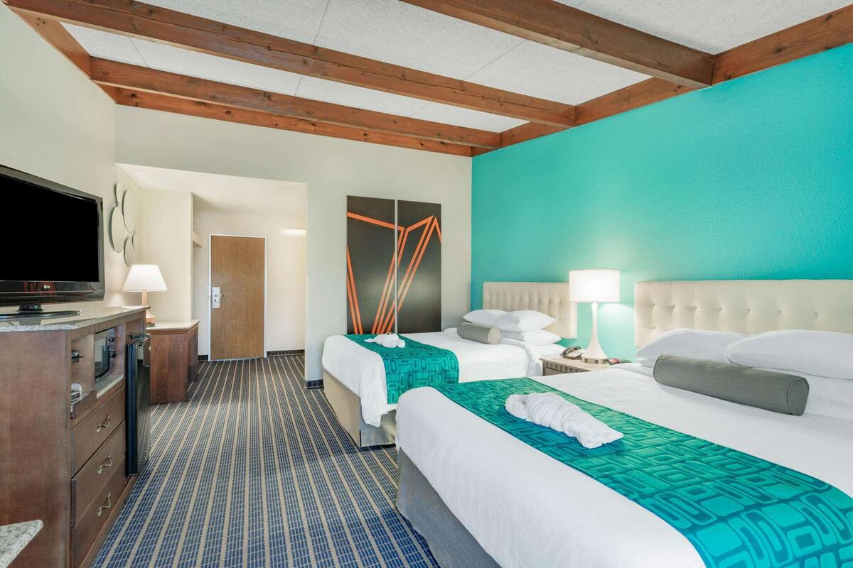 A hotel room with two beds, a television, a desk with a lamp, and a painting on the wall.
