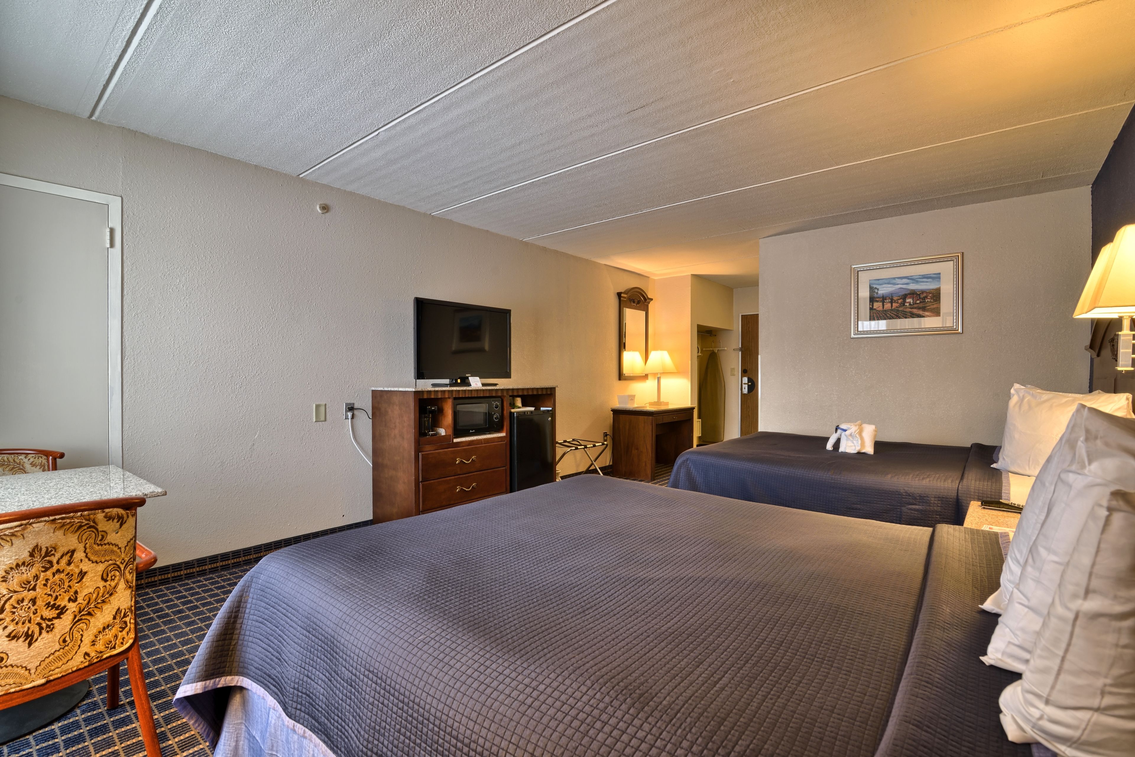 A hotel room with two beds, a desk, a microwave, a refrigerator, and a television.