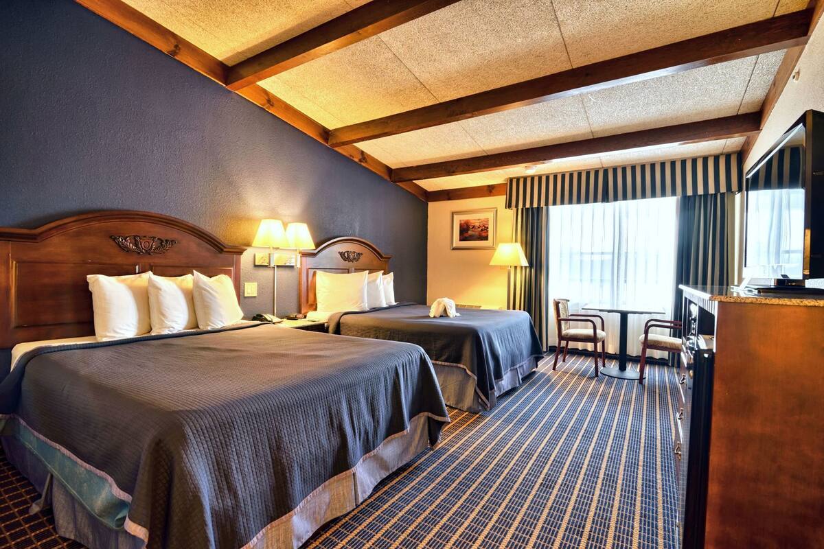 A hotel room with two beds, a desk, a chair, a television, and a window with curtains.