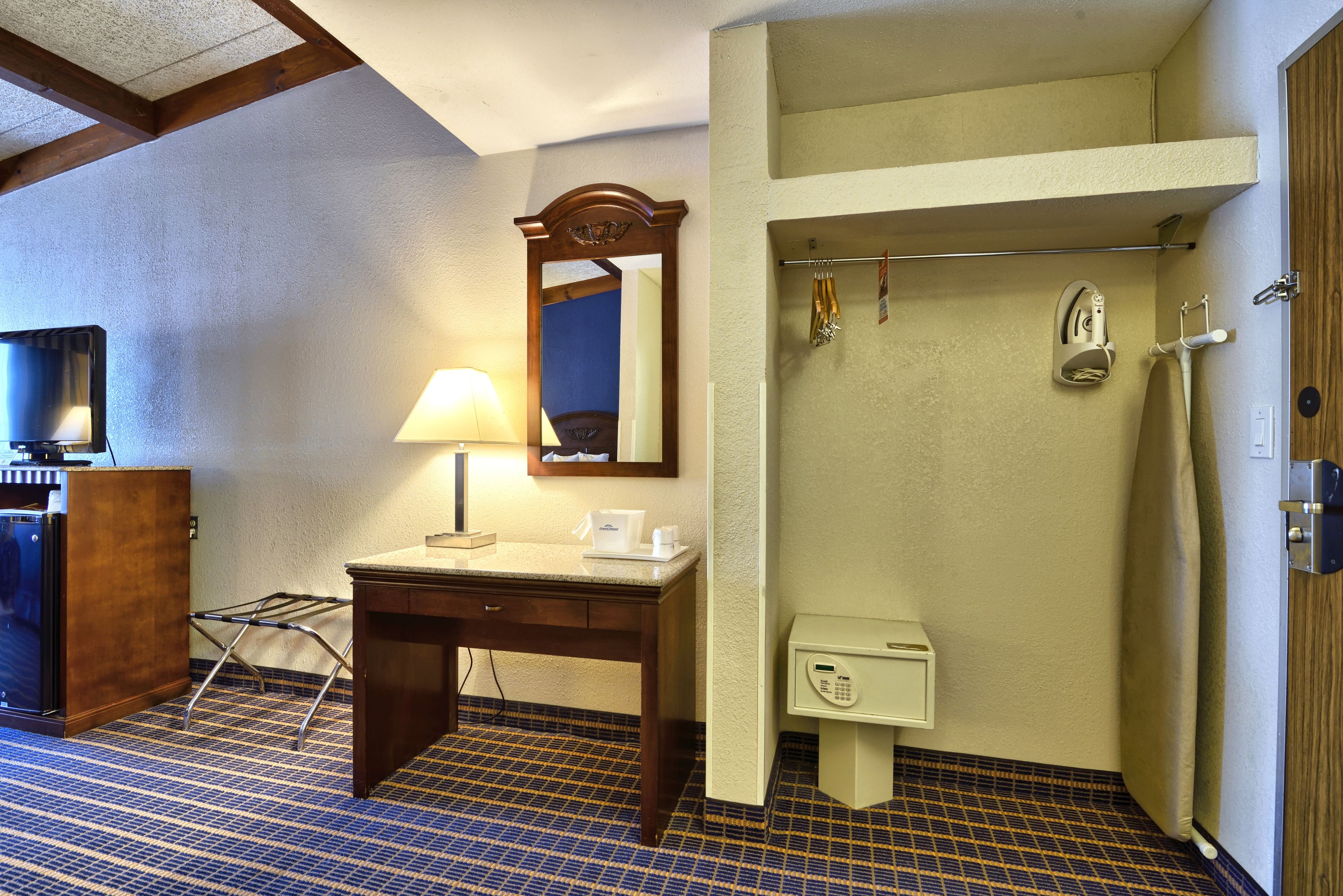 Camera d'albergo con una scrivania in legno, una lampada, uno specchio, un bagno piccolo con un portascopino e un telefono.