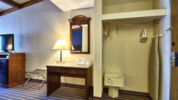 Camera d'albergo con una scrivania in legno, una lampada, uno specchio, un bagno piccolo con un portascopino e un telefono.