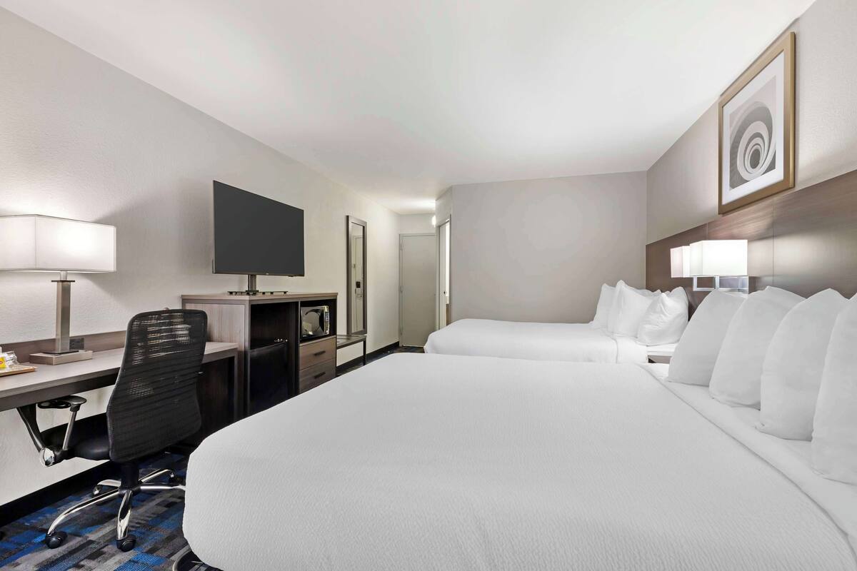 A hotel room with a large bed, a desk with a chair, a television, and a wall-mounted artwork.