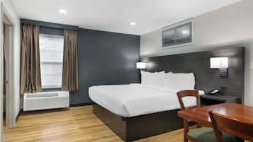 Una habitación de hotel con cama, escritorio, silla, lámpara y ventana con cortinas.