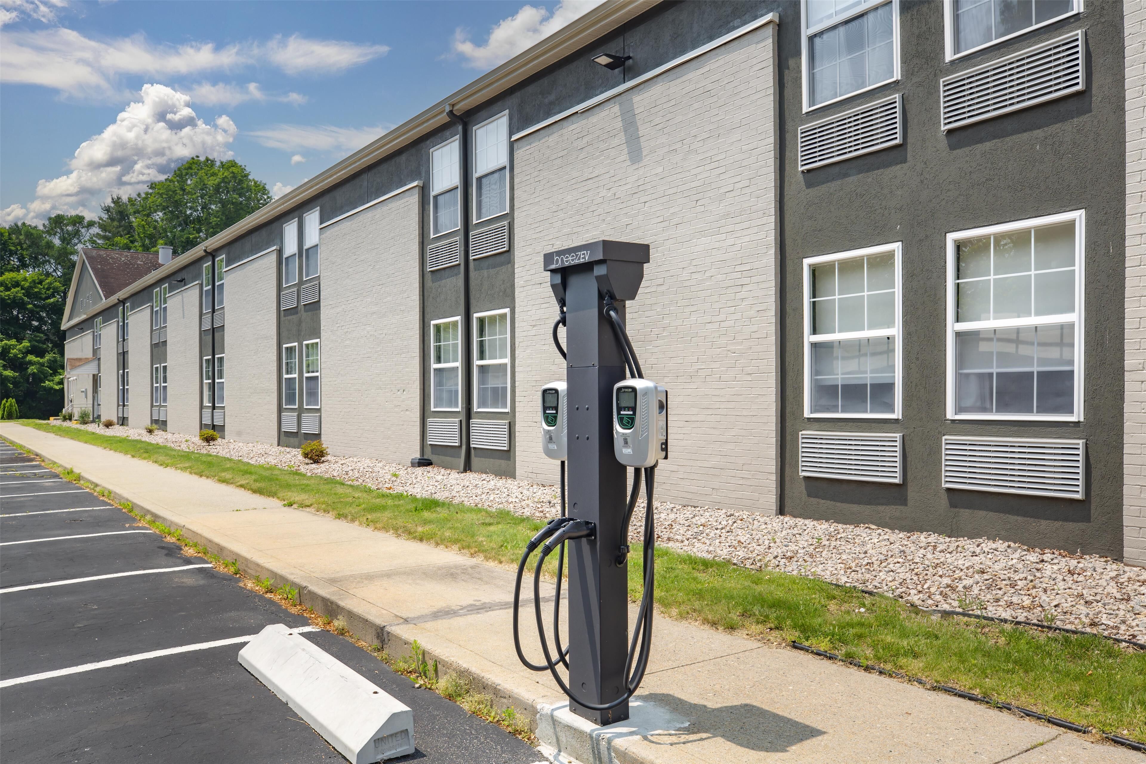 A parking lot with a row of buildings, a paved walkway, and a charging station.