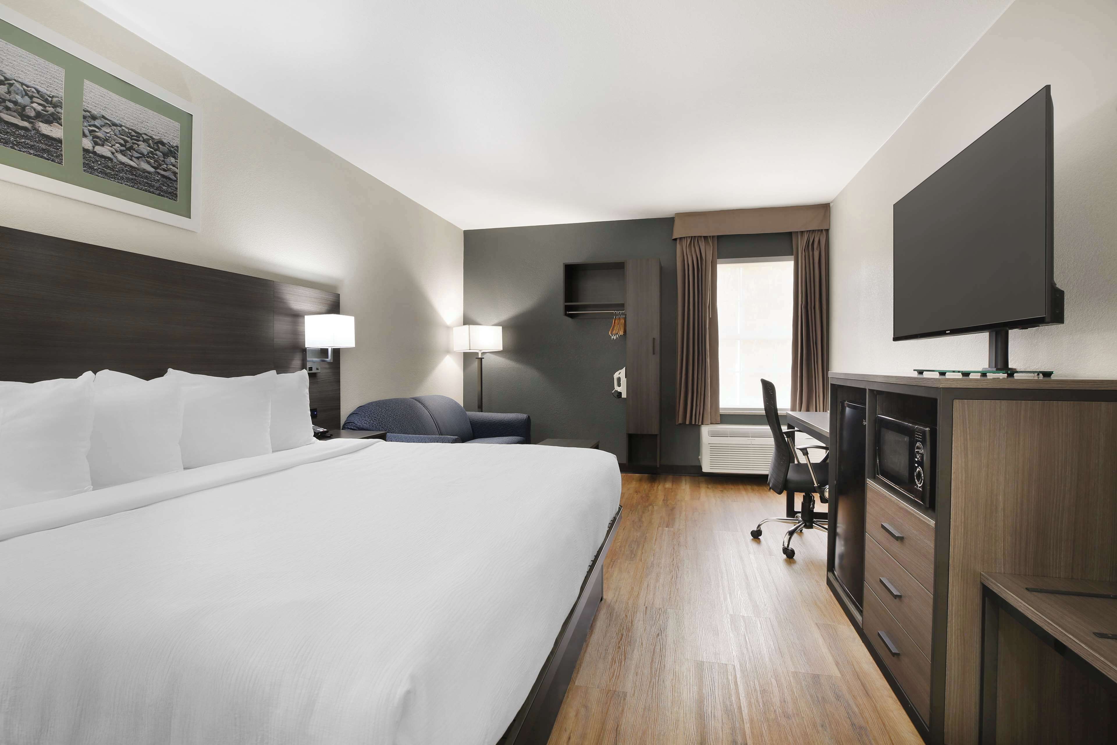 Quarto de hotel com uma cama grande, uma escrivaninha com computador, televisão de tela plana e uma janela com cortinas.