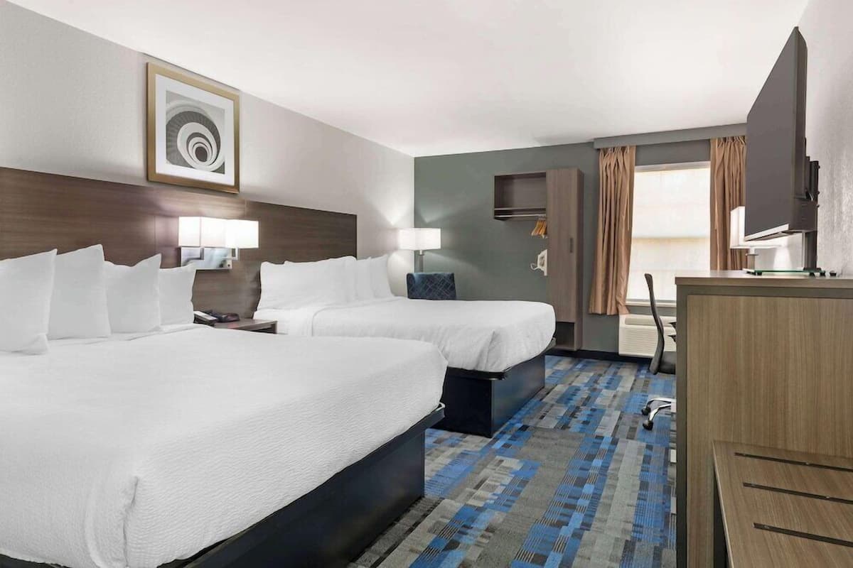 A hotel room with two beds, a desk, a chair, a TV, and a window with curtains.
