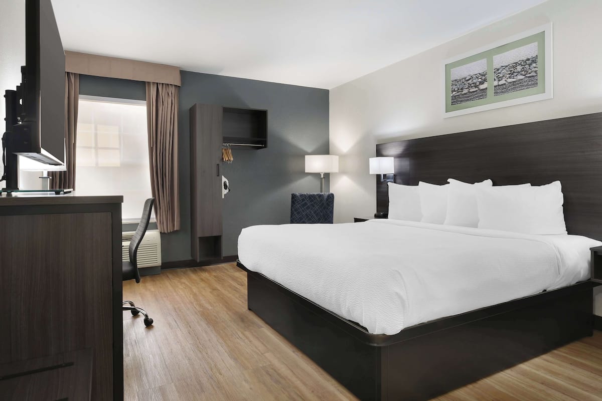 A hotel room with a large bed, a desk, a chair, a TV, and a window with curtains.
