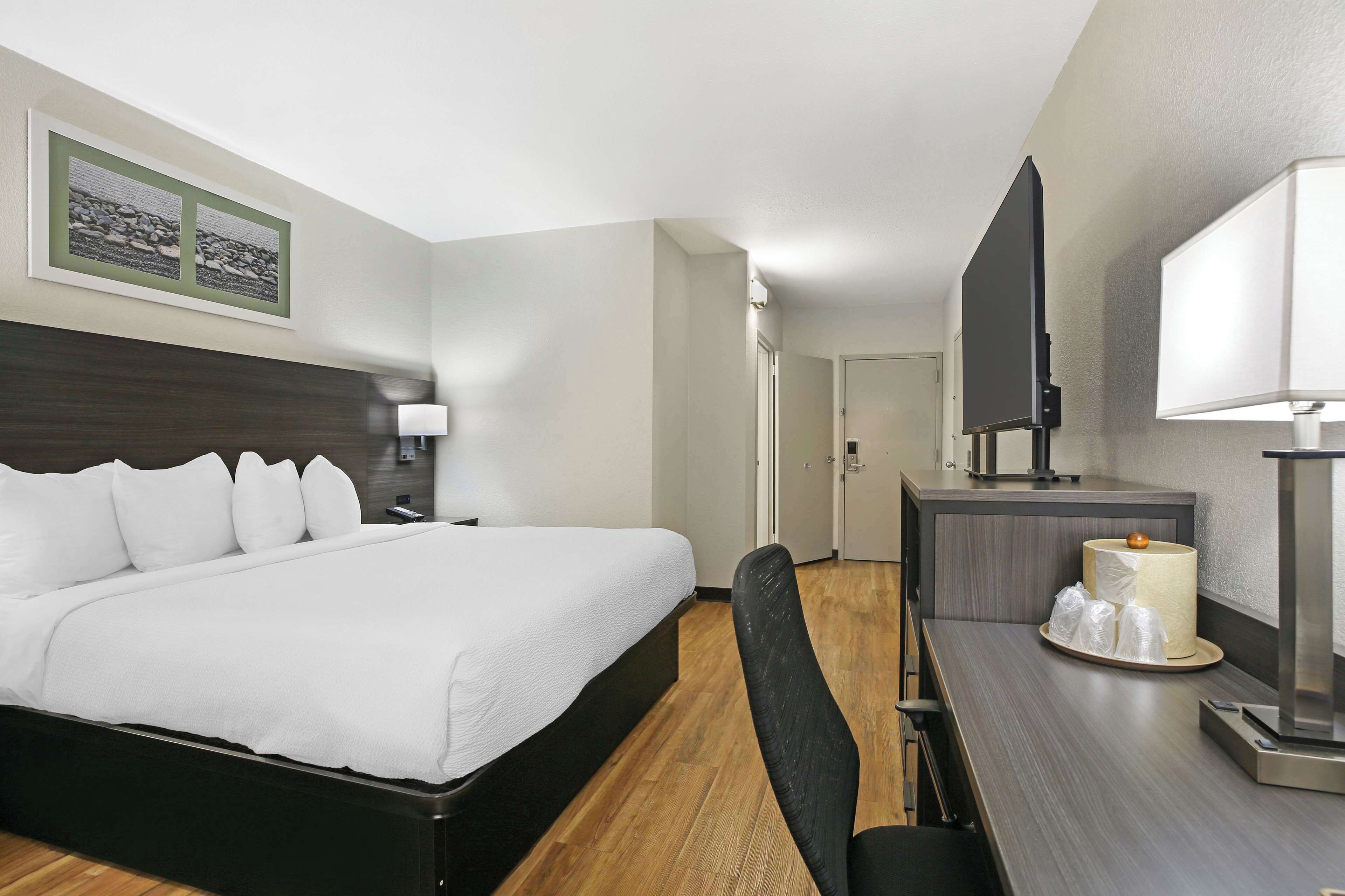 A hotel room with a large bed, a desk with a computer, a TV, and a lamp.