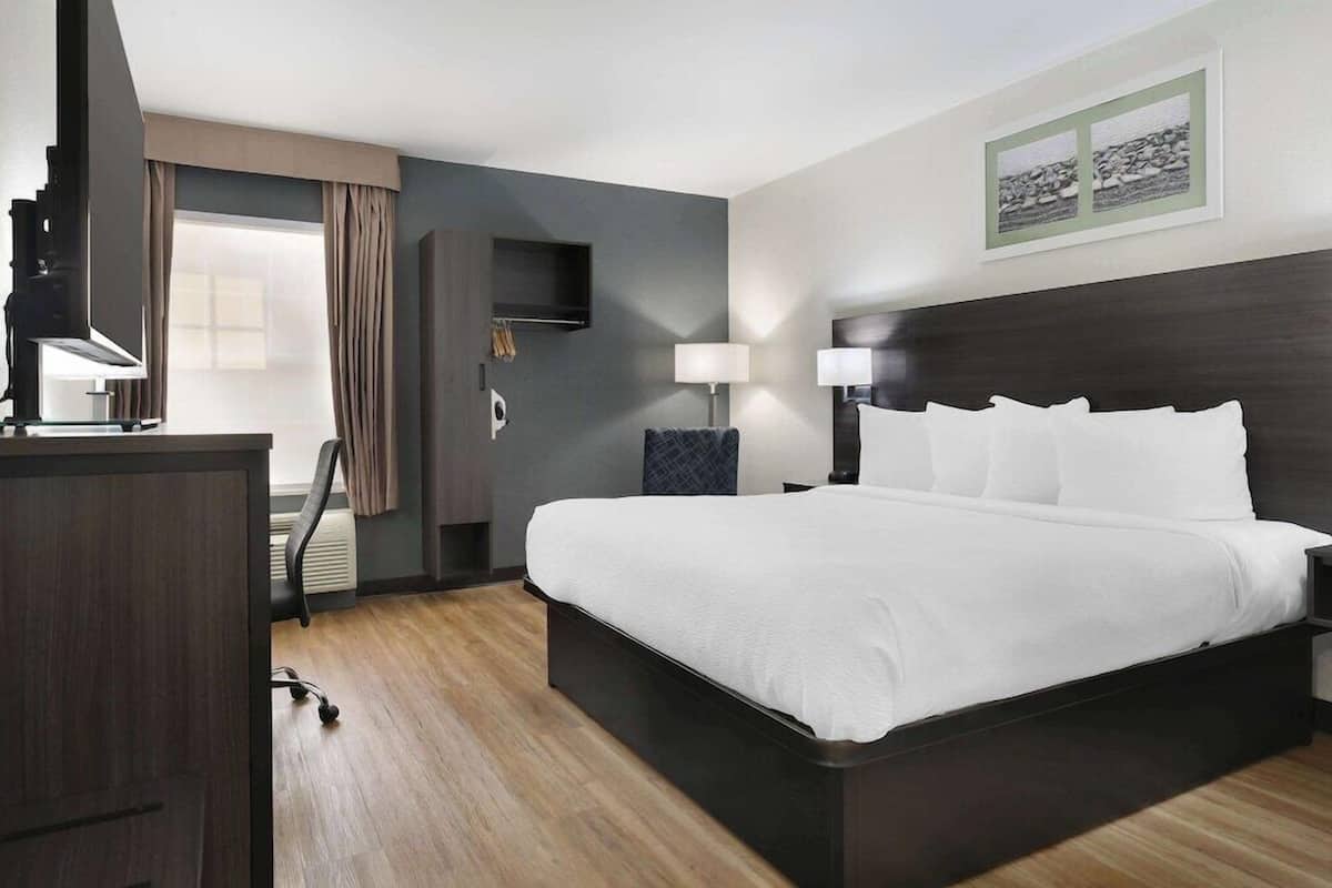 A hotel room with a large bed, a desk, a chair, a TV, and a window with curtains.