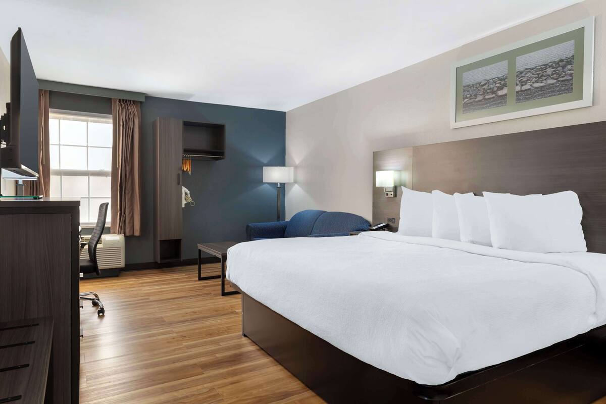 A hotel room with a large bed, a desk with a chair, a lamp, and a picture on the wall.