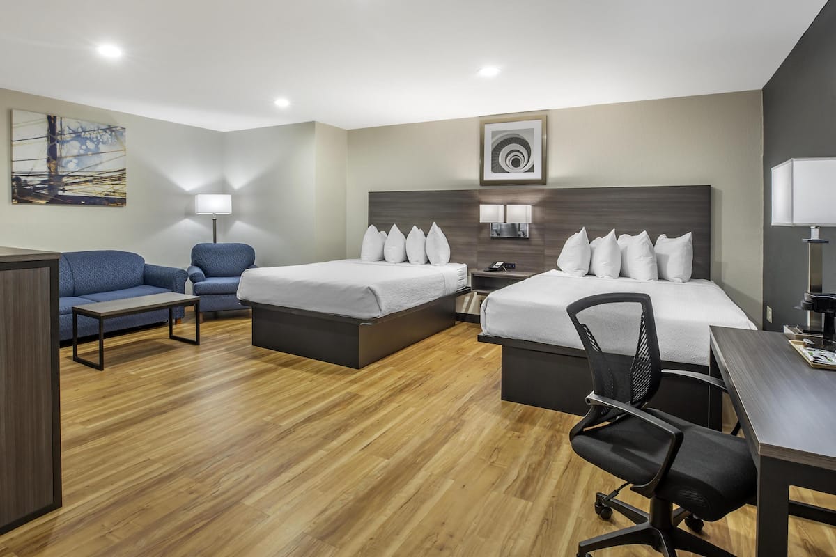 A hotel room with two beds, a desk, a chair, a sofa, and a lamp.