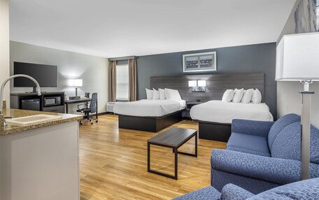 A hotel room with two beds, a desk, a chair, a small table, a TV, and a bathroom.