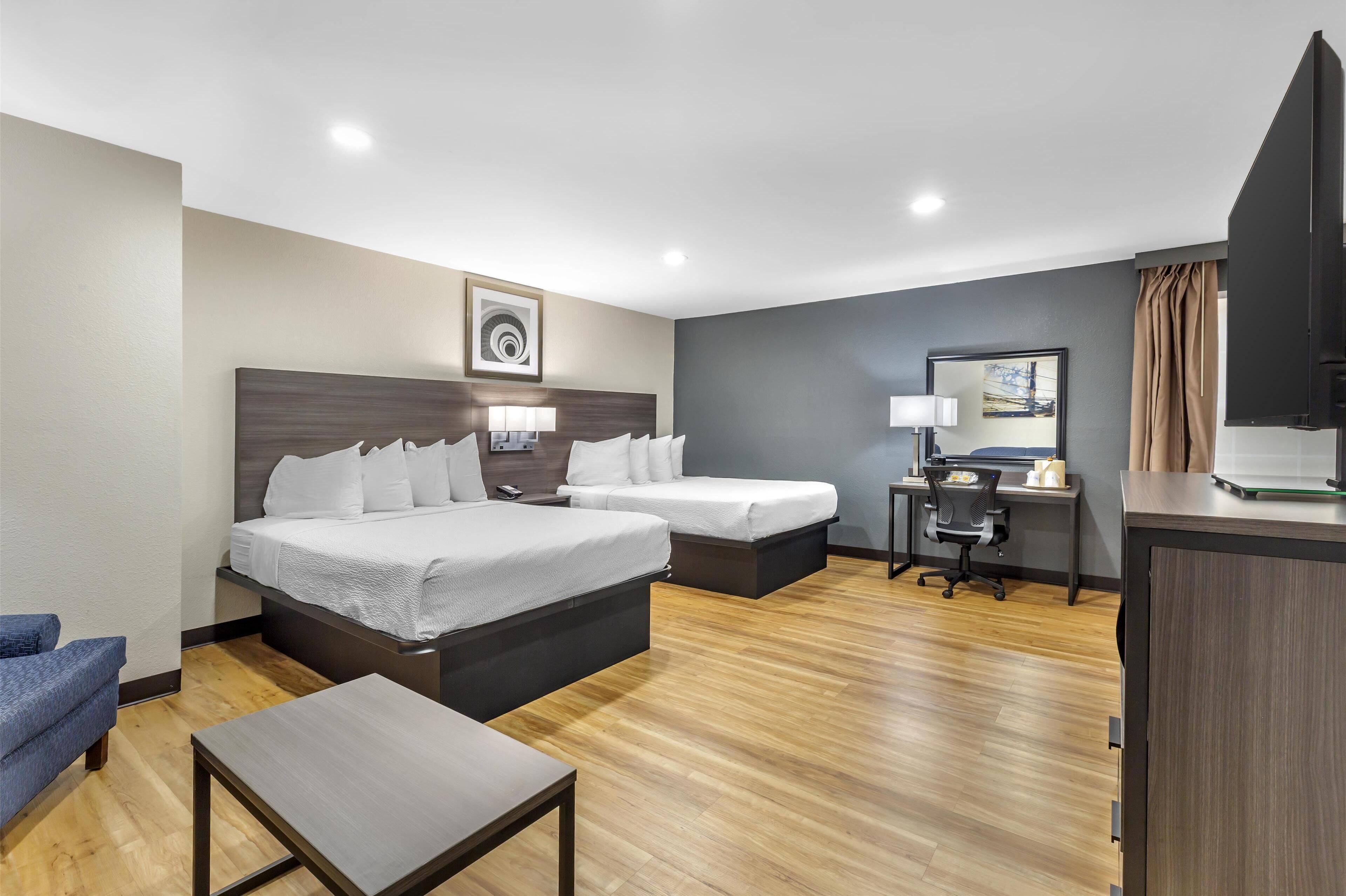 A hotel room with two beds, a desk, a chair, and a TV.