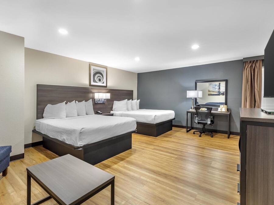 A hotel room with two beds, a desk, a chair, and a TV.