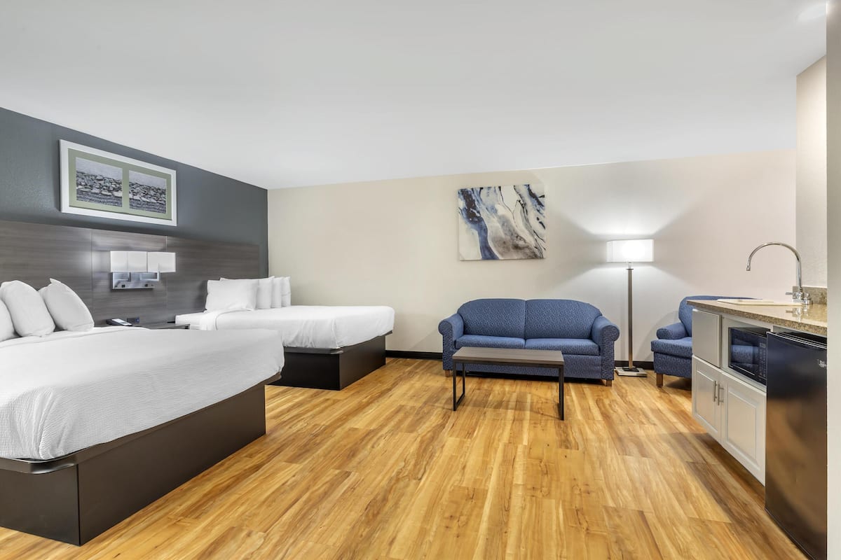 A hotel room with a bed, two bedside tables, a sofa, a desk, and a kitchenette.