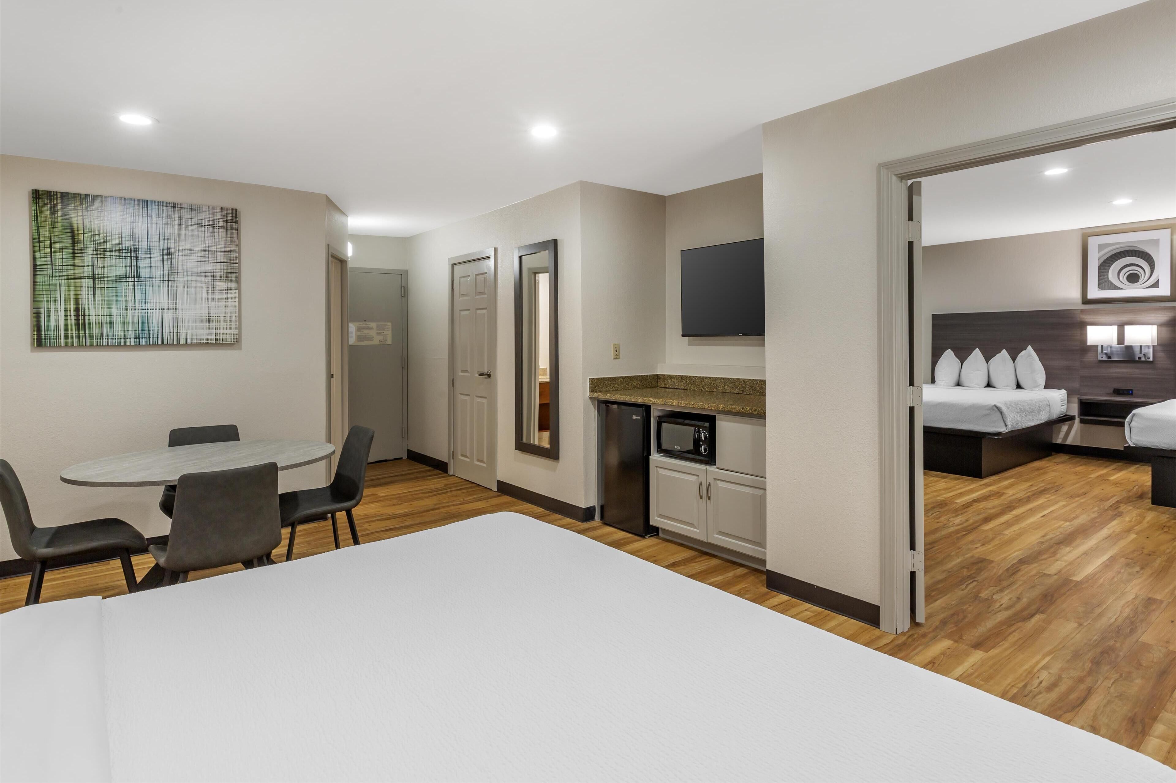 Une chambre d’hôtel moderne dotée d’un coin repas, d’une kitchenette et d’un espace nuit séparé avec un lit et une télévision.