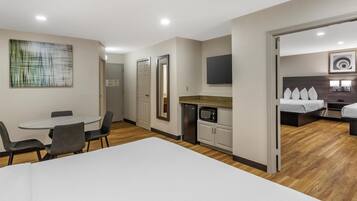Una habitación de hotel moderna con comedor, kitchenette y un área de descanso separada con cama y televisor.